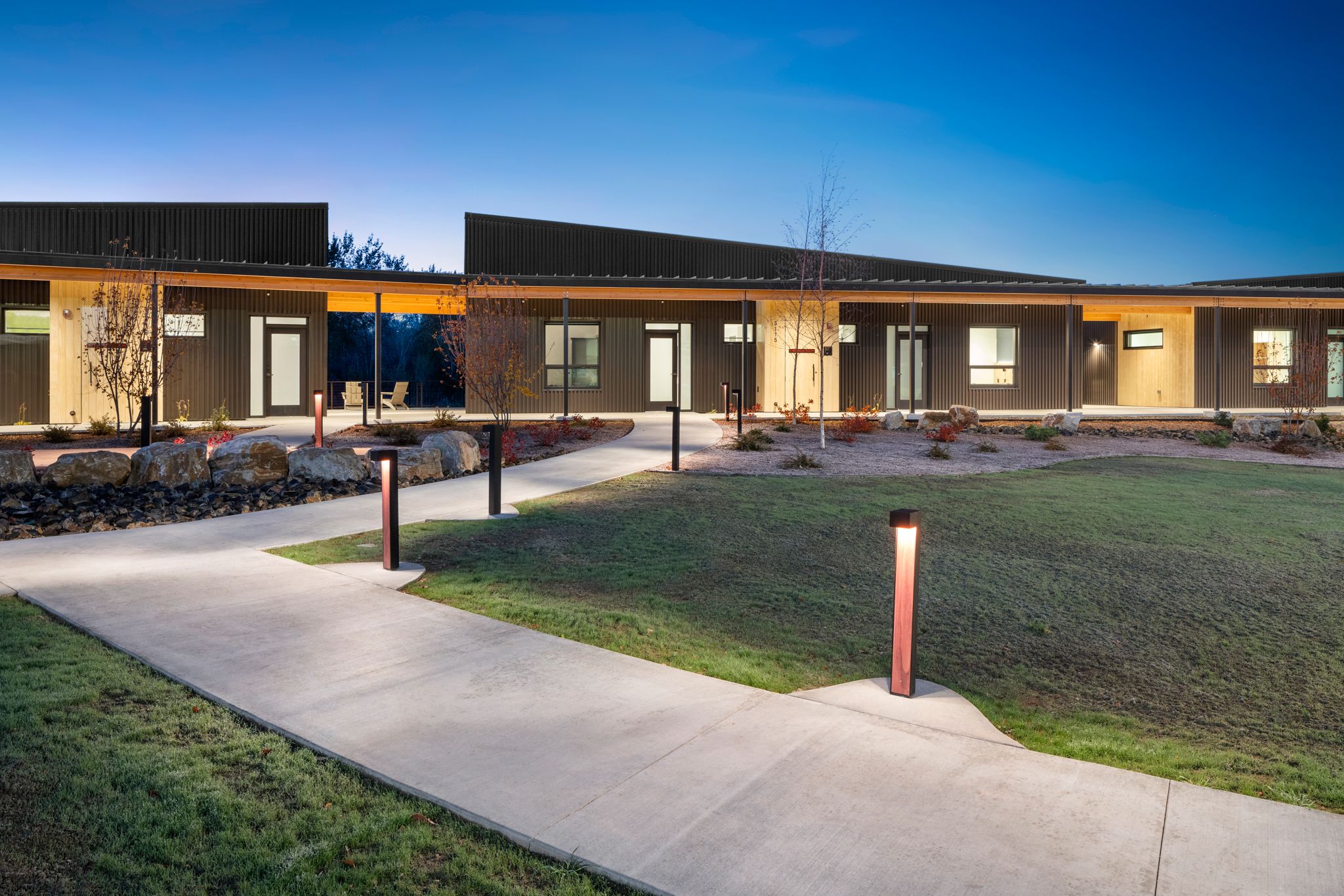 Exterior of the participant lodging buildings at dawn on the Idaho Outdoor Fieldhouse campus, with a soft morning light across the buildings and grounds.